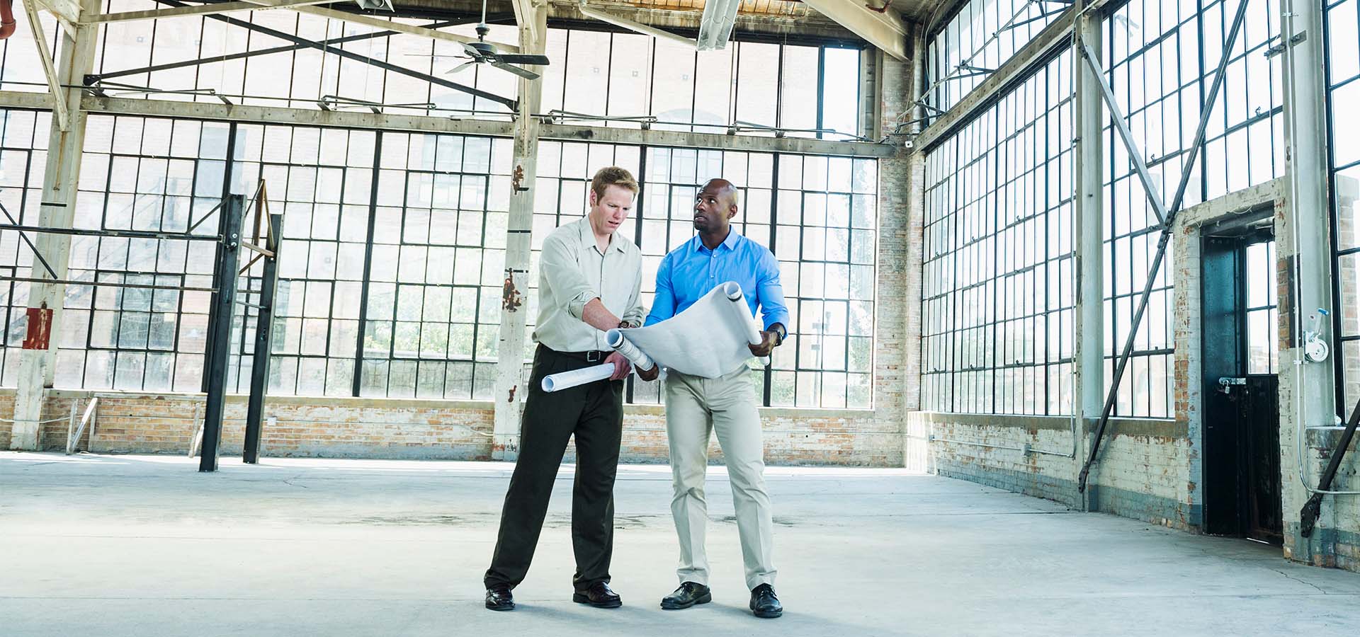 Two men look at blueprints inside a vacant building.