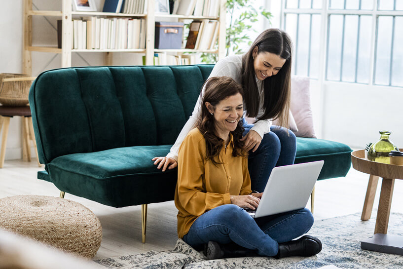 Two women smile as one works on a laptop computer.