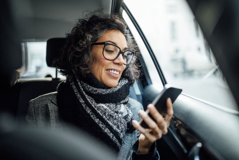 A woman riding in a car smiles as she looks at her mobile phone.